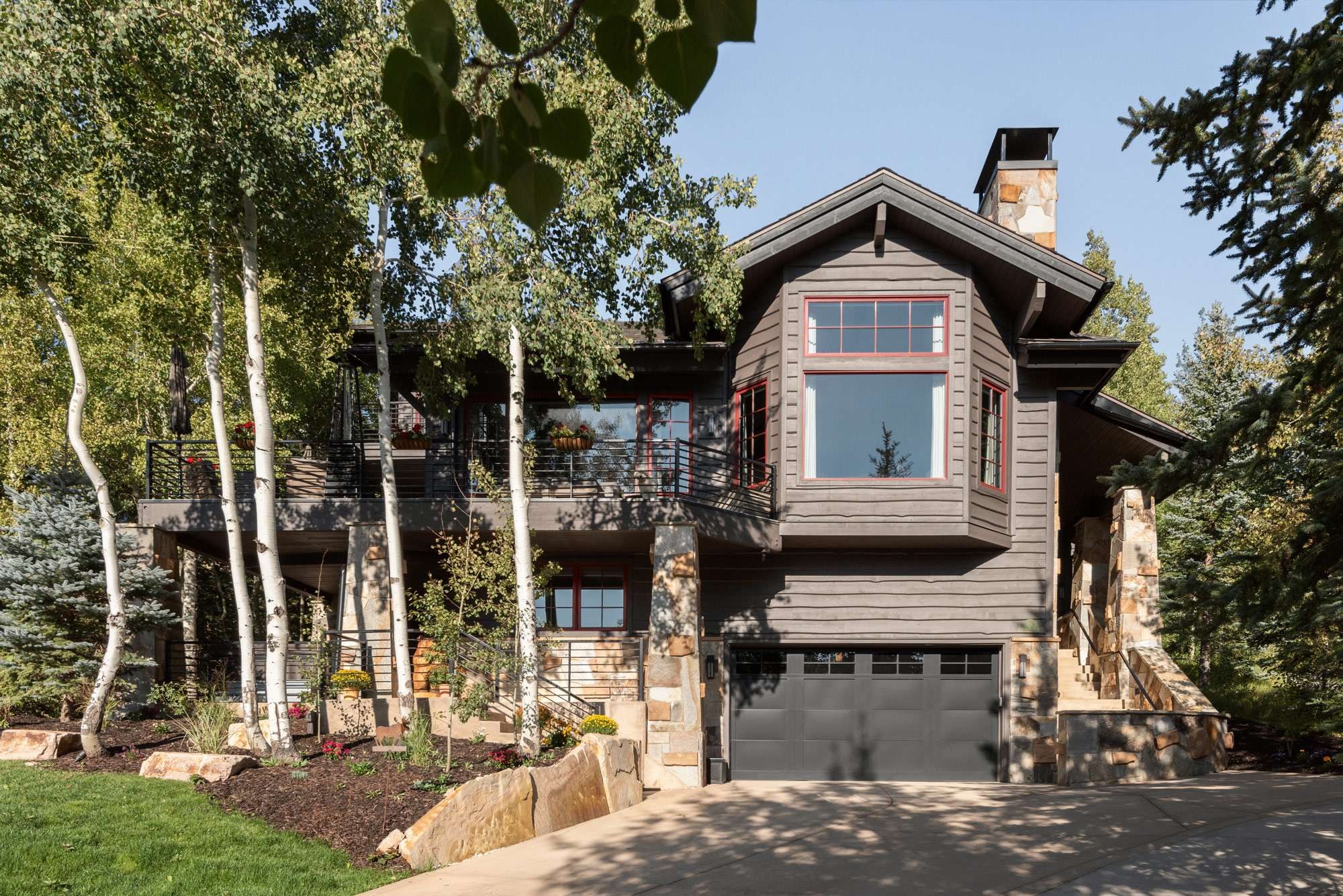 Bella House front elevation with dark timber siding, stone piers, and aspen groves