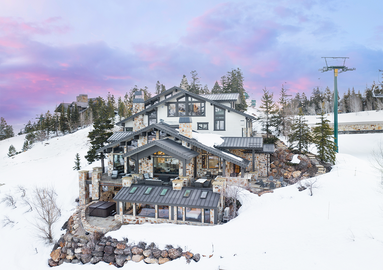 Snow-covered mountain chalet with stone piers and metal roofs at twilight