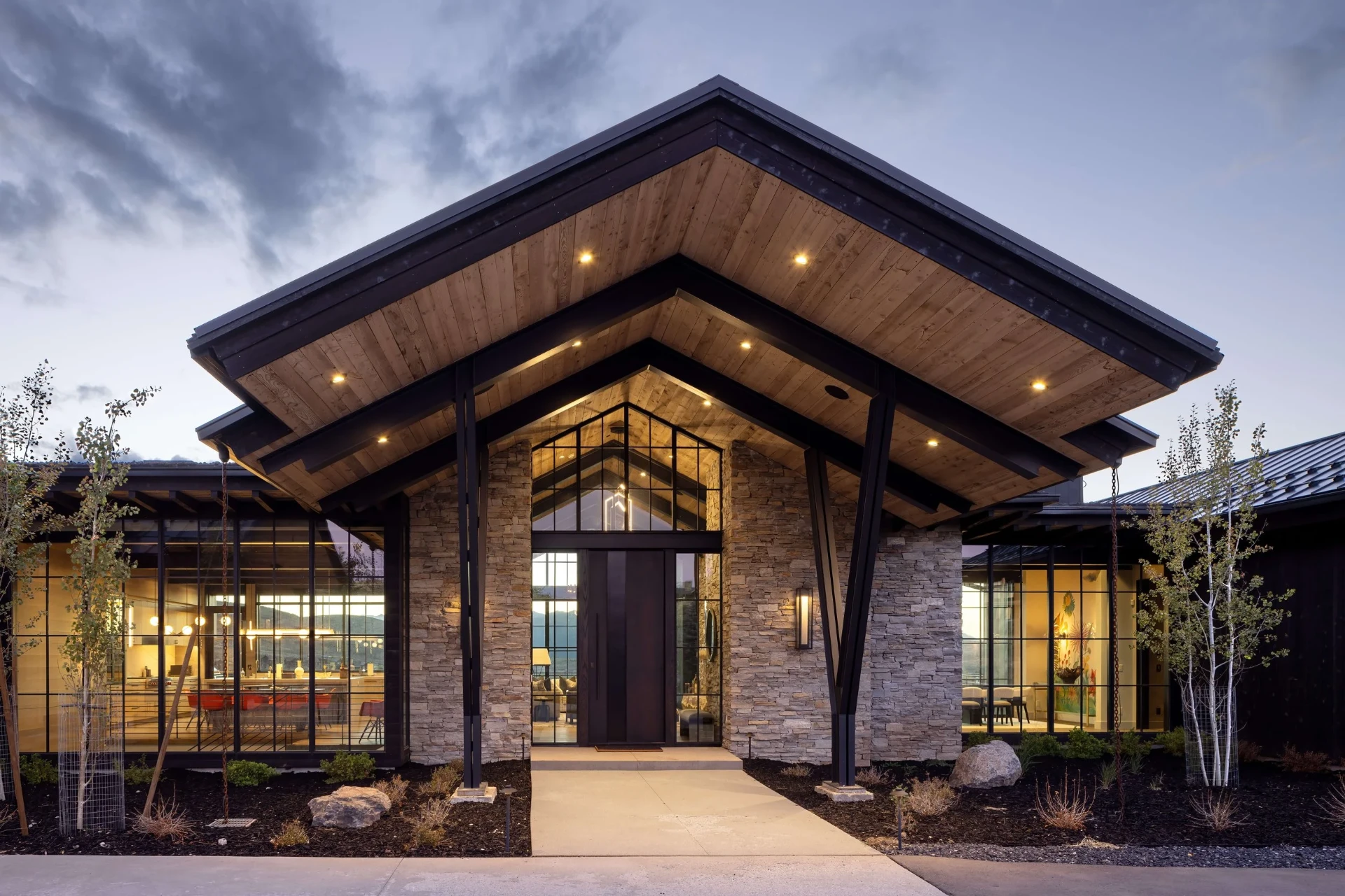 Ridgeview front entry at dusk under a timber-soffit gabled portico with dry-stack stone